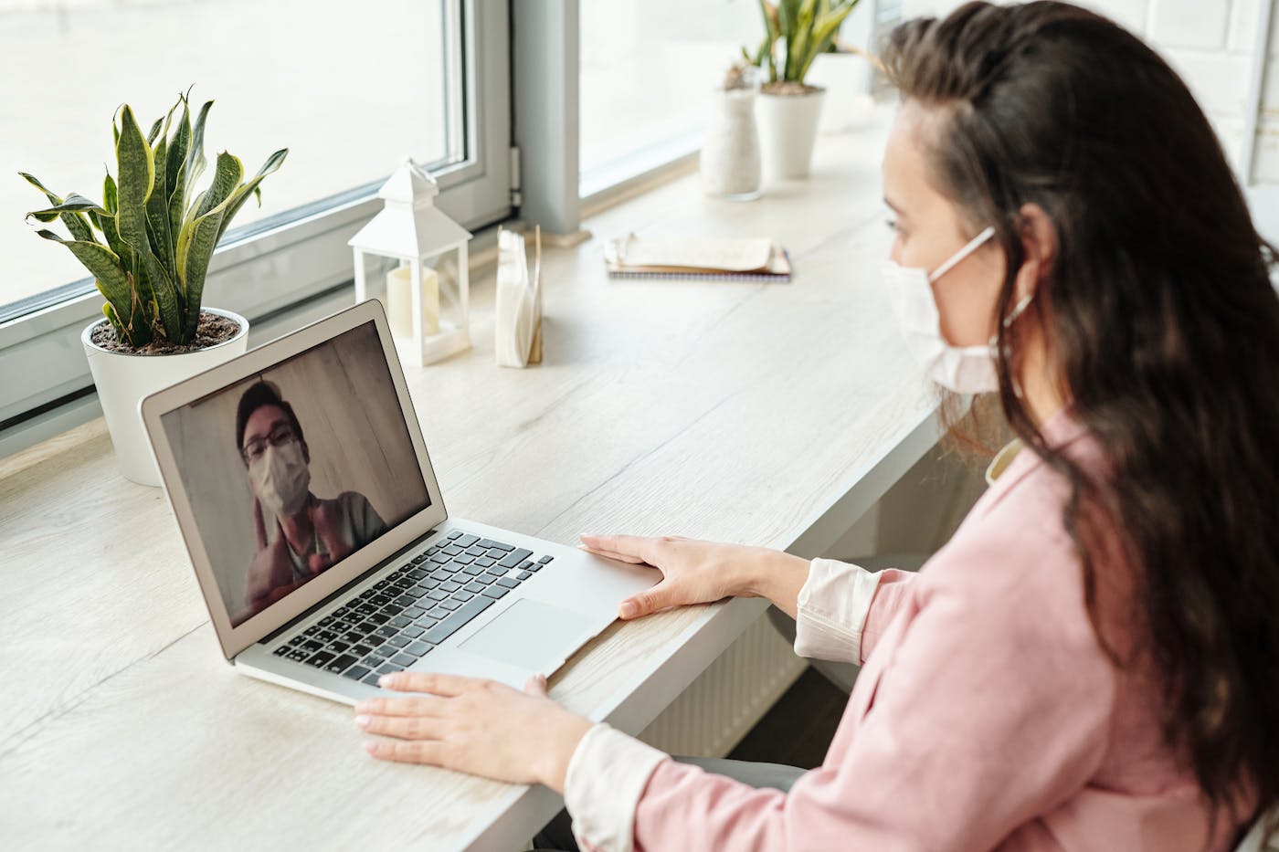 A patient at a laptop on a video call with a doctor on the screen.